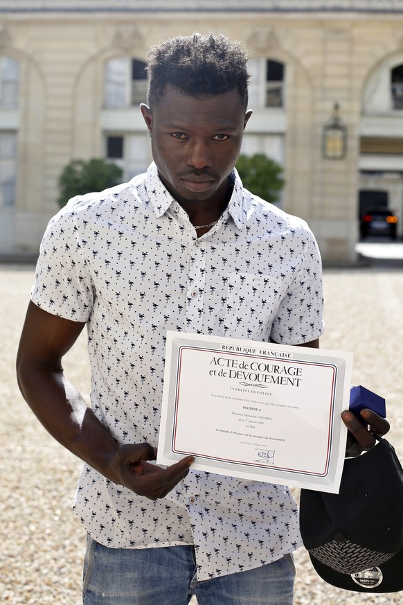 epa06768275 Mamoudou Gassama from Mali shows a certificate of courage and dedication signed by Paris Police Prefect Michel Delpuech as he leaves the presidential Elysee Palace after his meeting with F ...