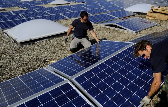Arbeiter installieren Solarpanelen auf dem Dach der Firma Debrunner AG, am Mittwoch, 24. April 2013, in Giubiasco. Nach Fertigstellung der Arbeiten werden die Solarpanelen eine Flaeche von 7000 Quadra ...