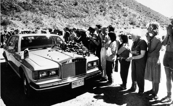 Indian spiritual leader Bhagwan Shree Rajneesh is greeted by thousands of his followers, sannyasins, during his afternoon drive-by as flowers are placed on the hood of his Rolls-Royce at his high dese ...