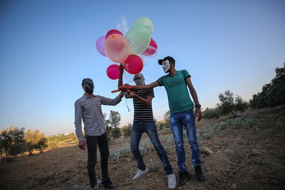 epa08599709 Palestinians wearing masks prepare to attach an incendiary device to balloons before realeasing them to Israeli lands near the border between Israel and Eastern Gaza Strip, Gaza Strip, 12  ...