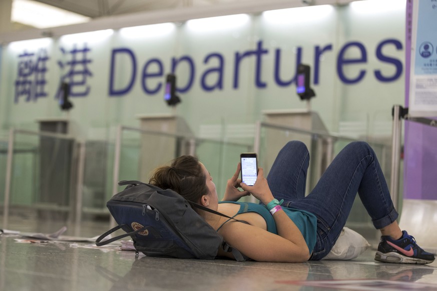 A traveler leans on her bag while browsing her smartphone at the departure hall of the Hong Kong International airport on Monday, Aug. 12, 2019. One of the world&#039;s busiest airports canceled all f ...