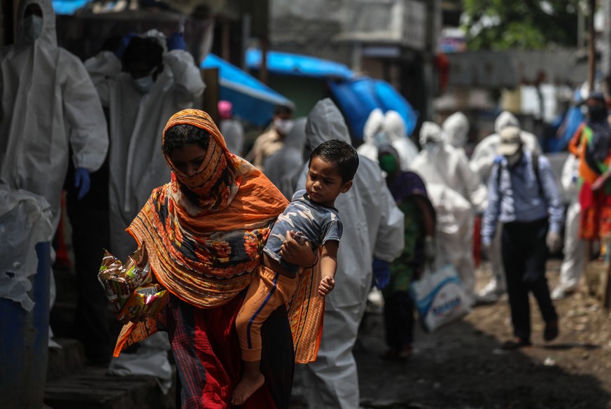 epa08538584 A woman carrying a toddler walks pass as the health workers wearing personal protective equipment (PPE) arrive to carry a medical checkup to the residents of a &#039;containment zones&#039 ...