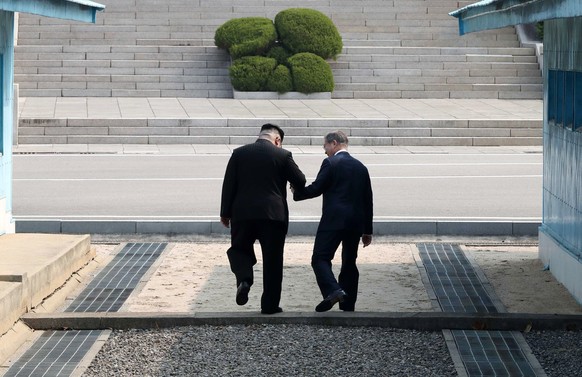 epaselect epa06695554 South Korean President Moon Jae-in (R) and North Korean leader Kim Jong-un (L) hold hands as they cross the military demarcation line (MDL) at the Joint Security Area (JSA) on th ...