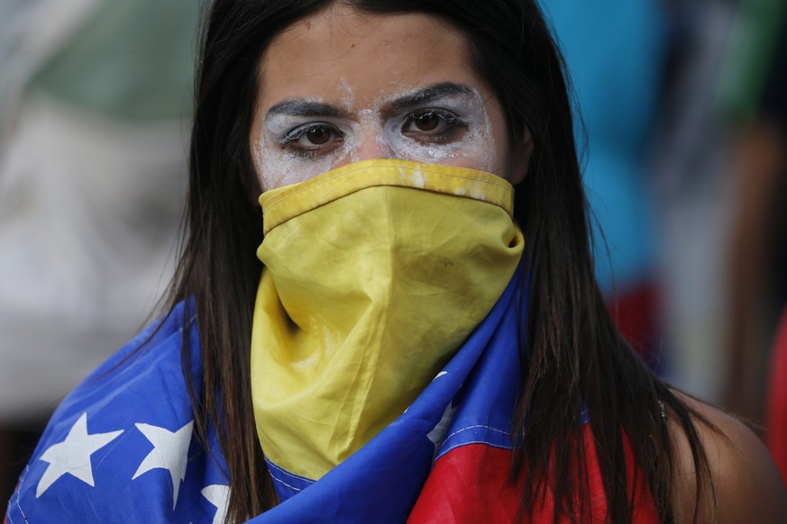 An anti-government protester covers her face with a Venezuelan flag, and uses toothpaste around her eyes to help lessen the effect of tear gas, during clashes with security forces after a rally demand ...