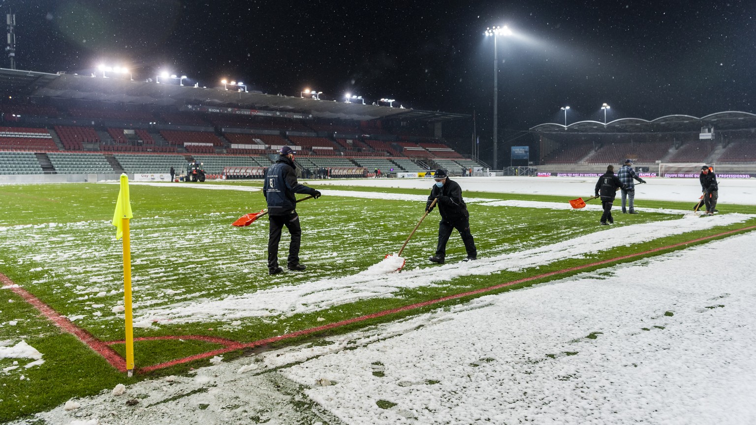 Des personnes enlevent la neige sur le terrain, lors de la rencontre de football a huis clos de Super League entre FC Sion et FC Luzern le samedi 12 decembre 2020 au stade de Tourbillon a Sion. (KEYST ...