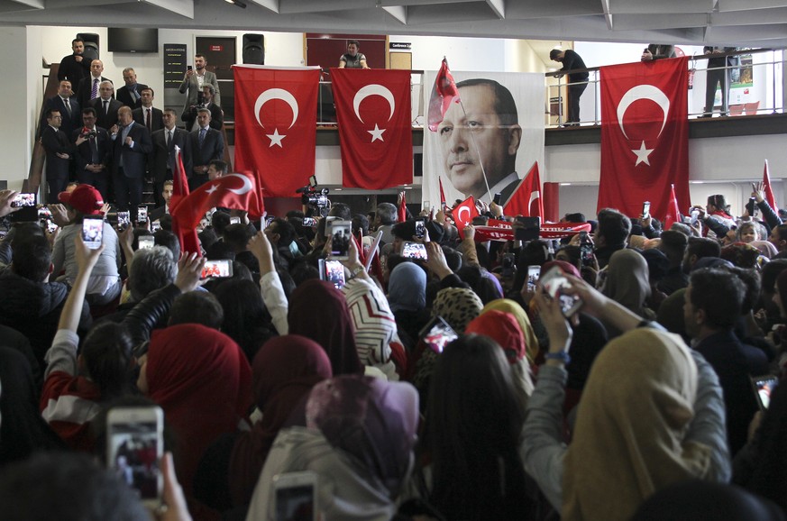 The pictures of Turkey&#039;s President Recep Tayyip Erdogan hangs on a balustrade among Turkish flags as Turkish Foreign Minister Mevlut Cavusoglu, center left, speaks during a campaign gathering in  ...