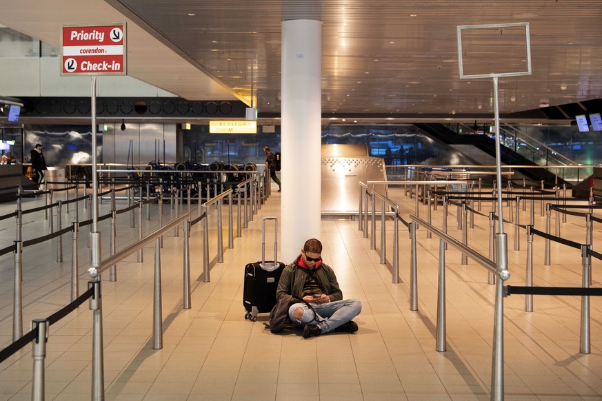 epaselect epa08292901 A traveler sits on the floor at a check-in counter at Schiphol Airport, the Netherlands, 13 March 2020. The Netherlands no longer allows incoming passenger flights from a number  ...