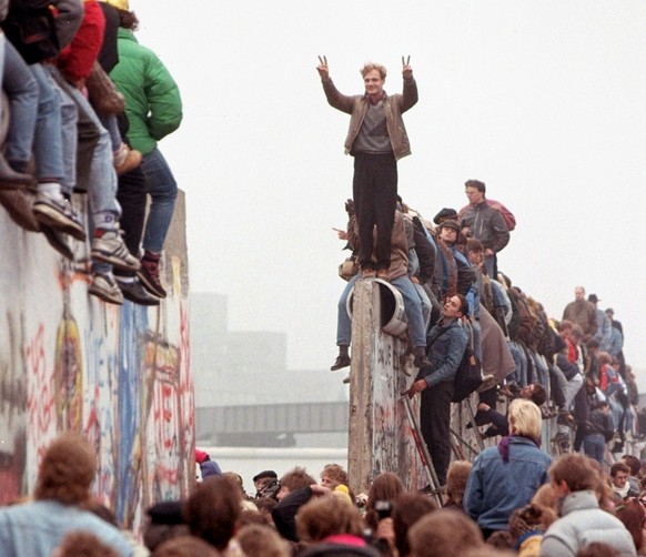 ** FILE ** Berliners celebrate on top of the wall as East Germans (backs to camera) flood through the dismantled Berlin Wall into West Berlin at Potsdamer Platz, in this November 12, 1989 file picture ...