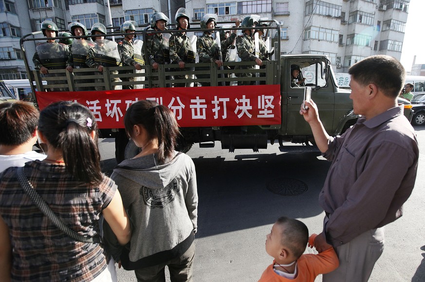 FILE - In this file photo taken Thursday, July 9, 2009, bystanders look at a truckload of paramilitary police with a banner which reads &quot;Determined crackdown on separatist activities&quot; patrol ...