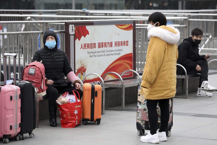 Travelers sit with their luggage outside the closed Hankou Railway Station in Wuhan in central China&#039;s Hubei Province, Thursday, Jan. 23, 2020. Overnight, Wuhan authorities announced that the air ...