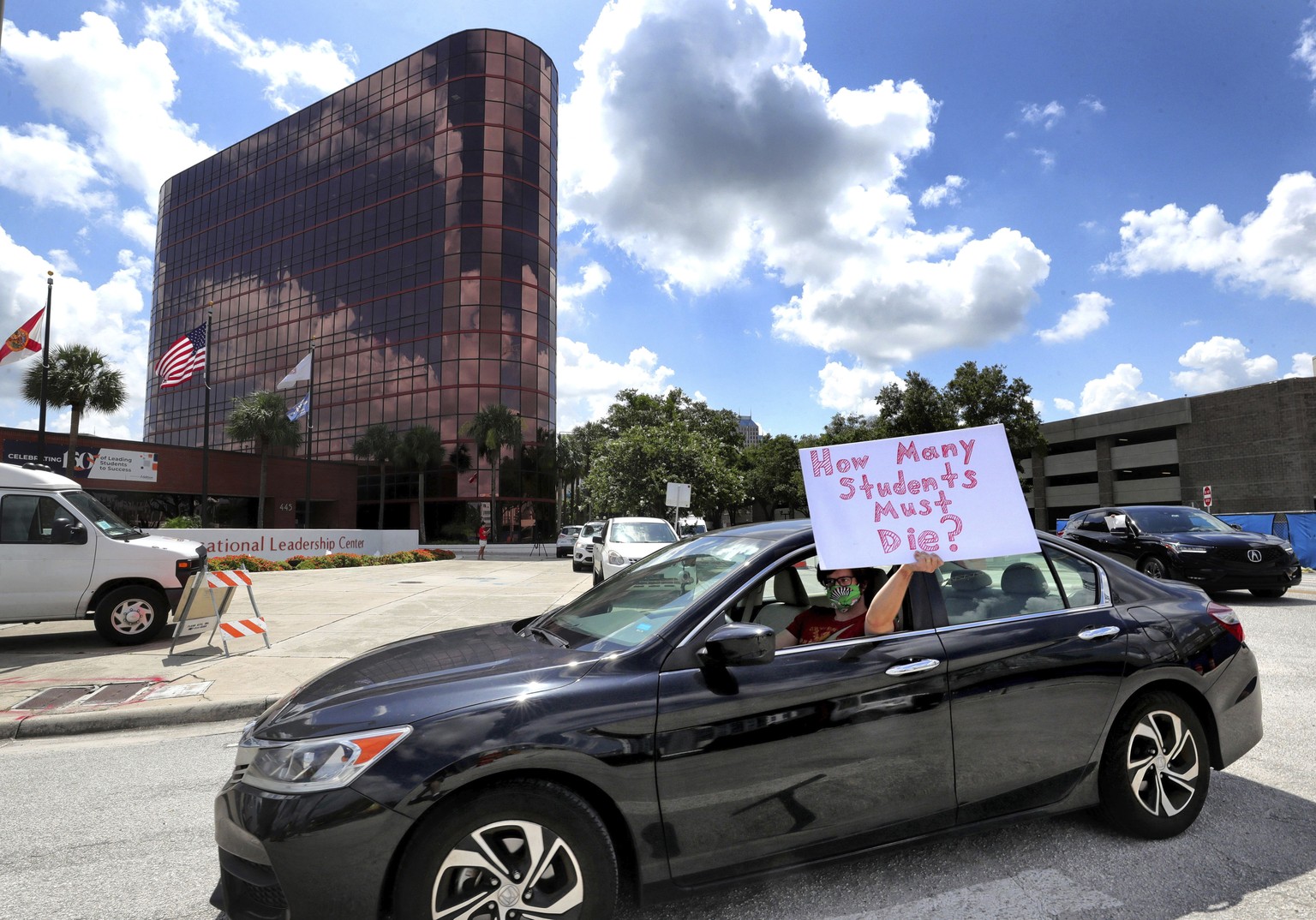 A teacher holds up a sign while driving by the Orange County Public Schools headquarters as educators protest in a car parade around the administration center in downtown Orlando, Fla., Tuesday, July  ...