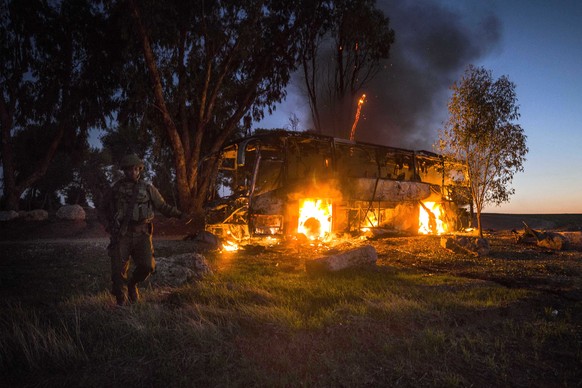 An Israeli soldier stands near a burning bus after it was hit by a mortar shell fired from Gaza near the Israel Gaza border, Monday, Nov. 12, 2018. Israel&#039;s military says it is prepared to step u ...