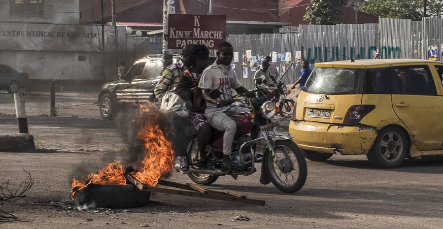 epa07242609 Motorists drive past tires set alight by opposition supporters after the electoral commission announced that the poll will be delayed by one week, in Kinshasa, Democratic Republic of the C ...