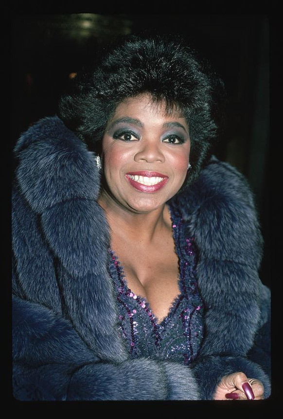 (Original Caption) : 1987: Headshot of Oprah Winfrey wearing a low-cut purple sequined dress and a fur coat. (Photo by LGI Stock/Corbis/VCG via Getty Images)