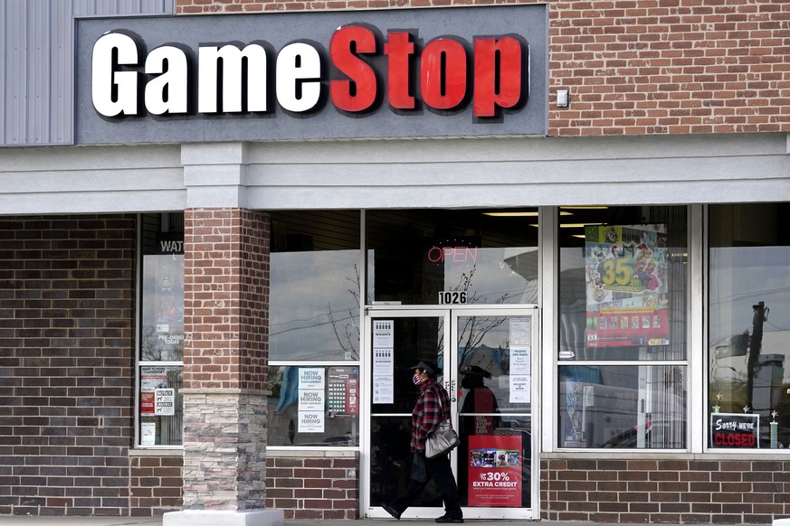 FILE - In this Oct. 15, 2020 file photo, a woman wears a face mask as she walks past a GameStop store in Des Plaines, Ill. Two hedge funds are bowing out of their short positions on the money-losing v ...