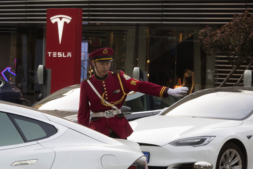 A security guard directs traffic near a Tesla charging station in Beijing, China, Tuesday, May 22, 2018. China said Tuesday it will reduce auto import duties effective July 1 following pledges to buy  ...