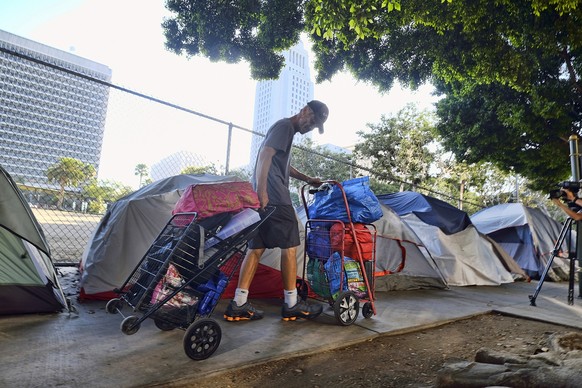 FILE - In this July 1, 2019, file photo, a homeless man moves his belongings from a street near Los Angeles City Hall, background, as crews prepared to clean the area. The city of Los Angeles has emba ...
