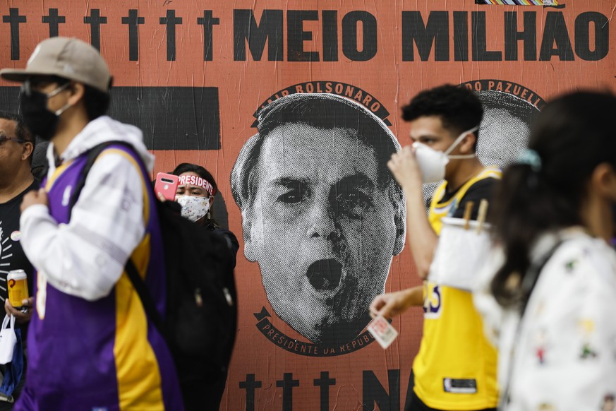 Demonstrators walk past a mural depicting the face of Brazilian President Jair Bolsonaro during a demonstration against Bolsonaro&#039;s handling of the coronavirus pandemic and economic policies prot ...