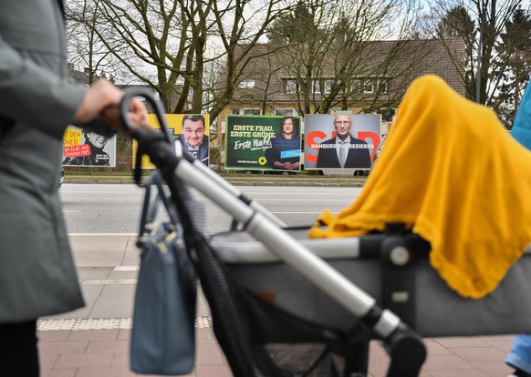 epa08225940 A woman pushes a baby buggy on a sidewalk opposite election posters of Hamburg&#039;s Green Party candidate for Mayor, Katharina Fegebank (L) and the leading candidate of the German Social ...