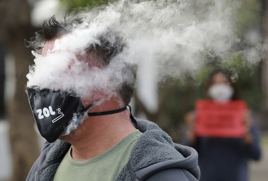 In this June 2, 2020 photo, a demonstrator exhales smoke while wearing a face mask during a protest against the tobacco ban outside parliament in Cape Town, South Africa. An effort to lift South Afric ...
