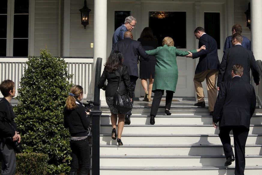 U.S. Democratic presidential candidate Hillary Clinton (in green coat, back to camera) loses her balance briefly as she arrives for a tour of SC STRONG, a home for ex-offenders and substance abusers o ...