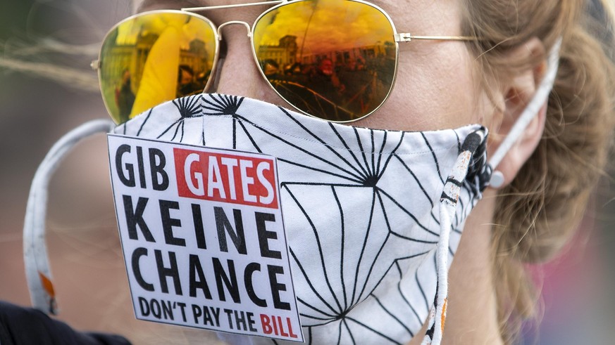 The Reichstag building, home of the German federal parliament, is mirrored in the glasses of a woman wearing a face mask with the slogan &quot;Don&#039;t Give (Bill) Gates A Chance&quot; during a demo ...