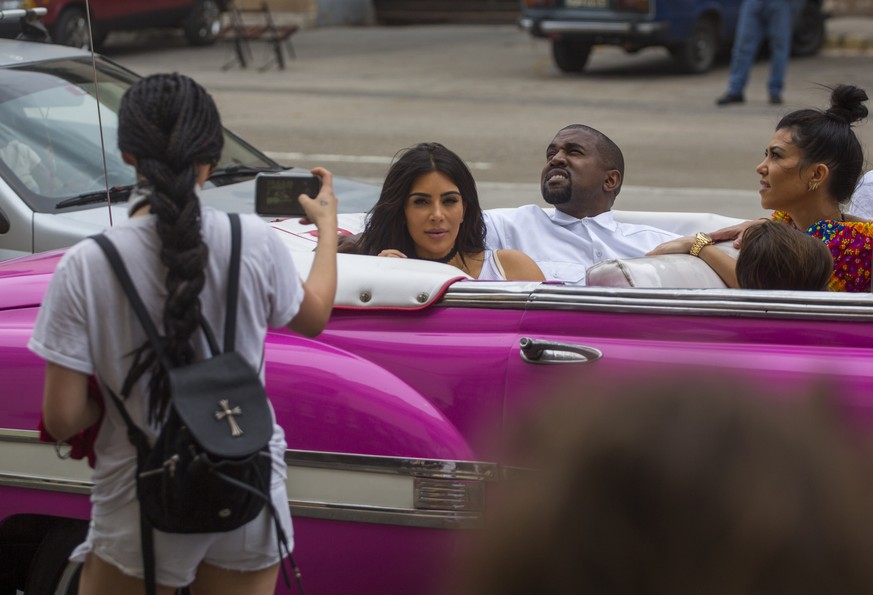 A woman uses her cellphone to take a picture American reality-show star Kim Kardashian West, center, and her husband Kayne West as they ride on a classic car along the streets of Havana, Cuba, Wednesd ...