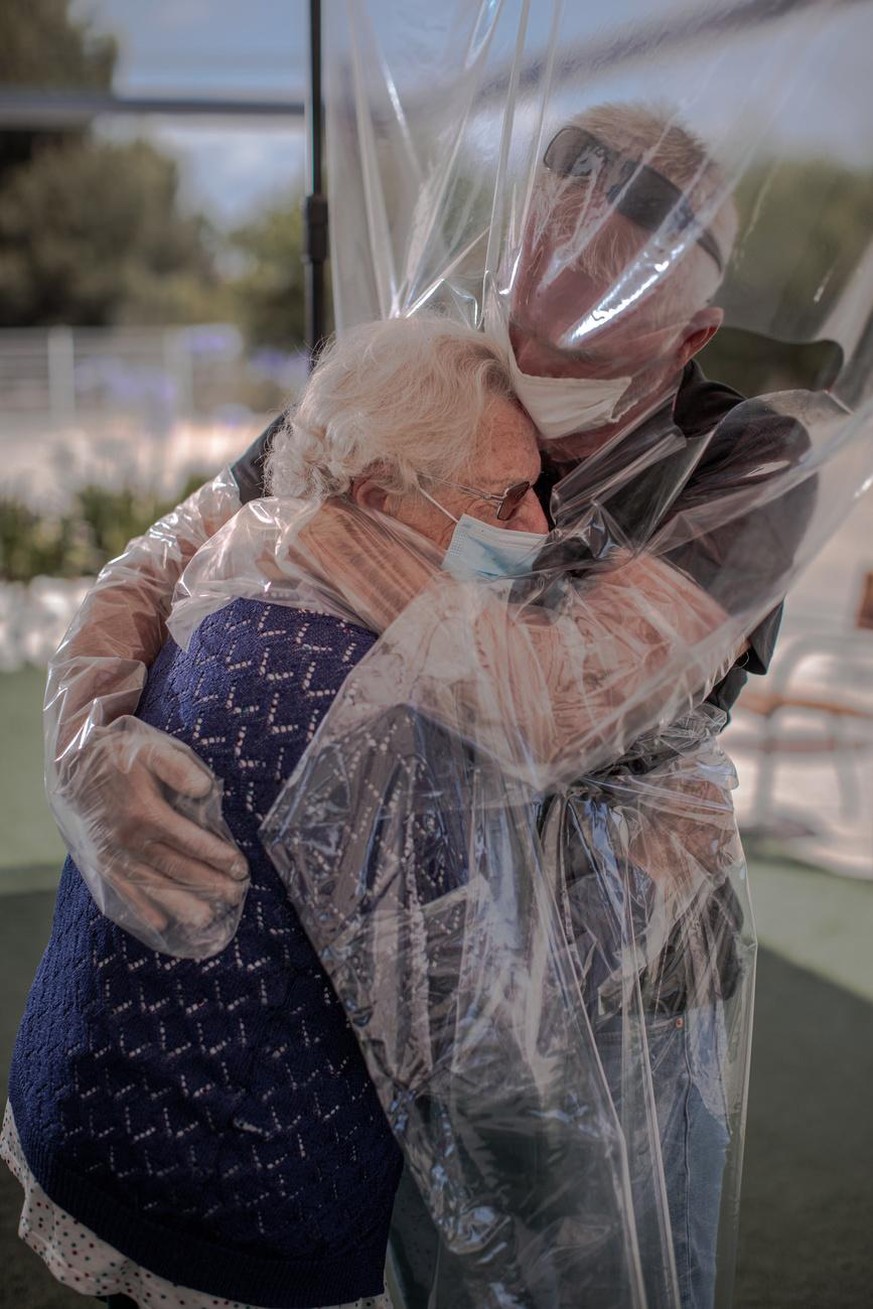 epa08490431 A woman (L) embraces her son (R) through a plastic device after three months without a hug at a home for the elderly in Valencia, Spain, 17 June 2020, amid the ongoing coronavirus pandemic ...
