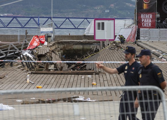 Two police officers walk at the scene the day after an oceanside boardwalk collapsed, in Vigo, Spain, Monday, Aug. 13, 2018. An oceanside boardwalk collapsed during a nighttime concert in the Spanish  ...