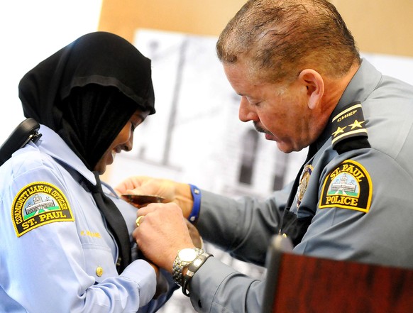 ADVANCE FOR USE MONDAY, SEPT. 15, 2014, AND THEREAFTER- In this March 1, 2014 photo, St. Paul, Minn. Community Officer Kadra Mohamed, left, smiles as she receives her badge from St. Paul, Minn. Police ...