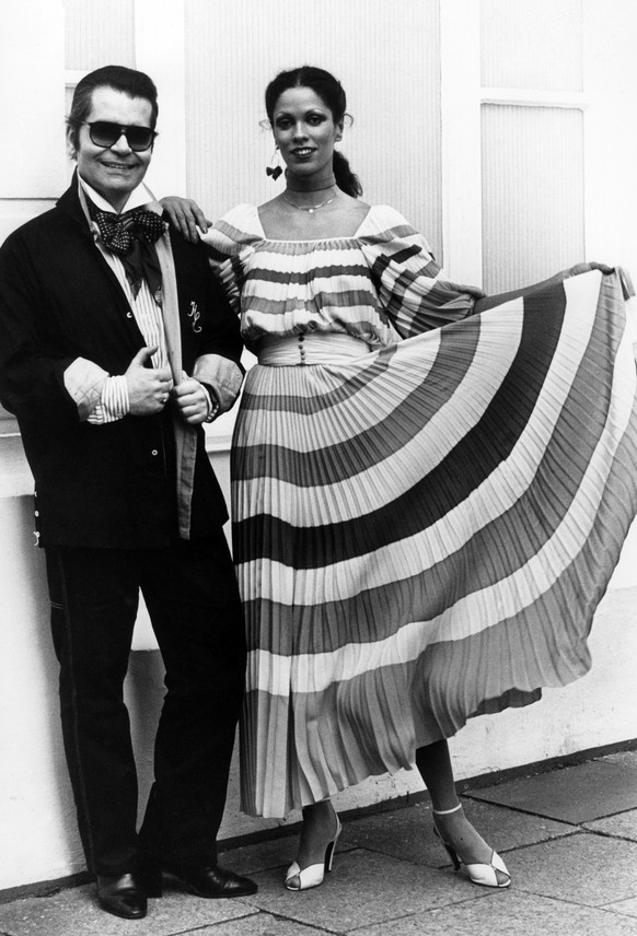 ARCHIV - 02.05.1977, Hamburg: Modeschoepfer Karl Lagerfeld neben einem Model in einem Plissee-Kleid aus Lagerfelds Chloe-Kollektion. Der deutsche Modeschoepfer Karl Lagerfeld ist gestorben. Das teilte ...