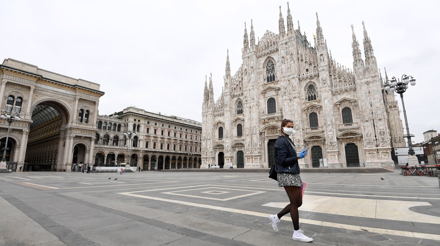 epa08289573 A tourist wearing a protective fave mask walks in Piazza Duomo (Cathedral Square), in Milan, Italy, 12 March 2020. Tougher lockdown measures kicked-in in Italy on the day after Italian Pre ...