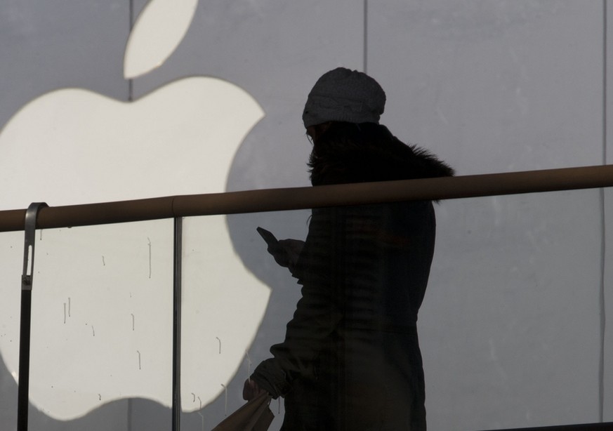 A woman using a phone walks past Apple&#039;s logo near its retail outlet in Beijing Monday, Dec. 23, 2013. Apple and China Mobile announced a long-anticipated agreement Monday to bring the iPhone to  ...