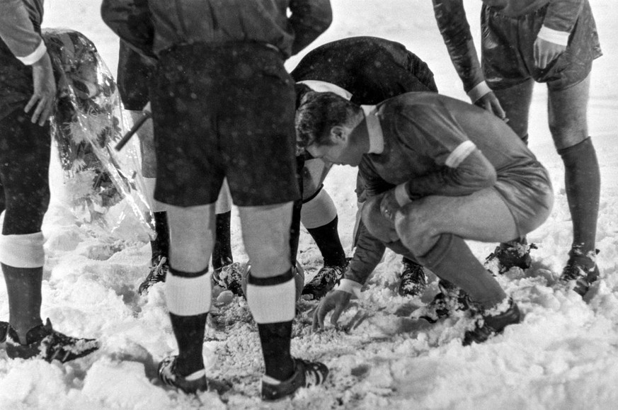 Schiedsrichter und der Captain der St. Galler suchen nach dem Muenzwurf bei der Platzwahl im zehn Zentimeter hohen Schnee nach der Muenze, aufgenommen am 26. November 1969. Das Rueckspiel der zweiten  ...