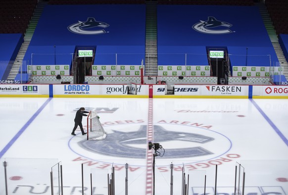 FILE - An arena worker removes the net from the ice after the Vancouver Canucks and Calgary Flames NHL hockey game was postponed due to a positive COVID-19 test result, in Vancouver, British Columbia, ...