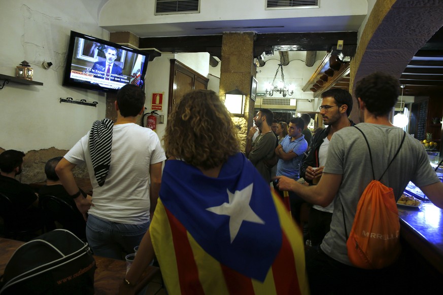 People, one of them with a Catalan independence flag around her shoulders, watch Spain&#039;s King Felipe&#039;s statement to the country about the situation in Catalonia on TV downtown Barcelona, Spa ...
