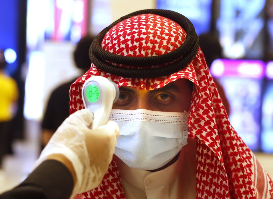 A Saudi cinema viewer has his temperature taken as he wears a face mask to help curb the spread of the coronavirus, at VOX Cinema hall in Jiddah, Saudi Arabia, Friday, June 26, 2020, after the announc ...