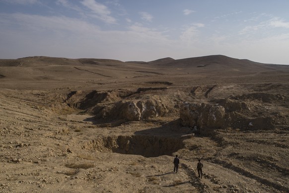 In this Nov. 11, 2017 photo, two Iraqi men walk near a sinkhole known as Khasfa, that is believed to contain the remains of people executed by Islamic State militants south of Mosul, Iraq. IS fighters ...