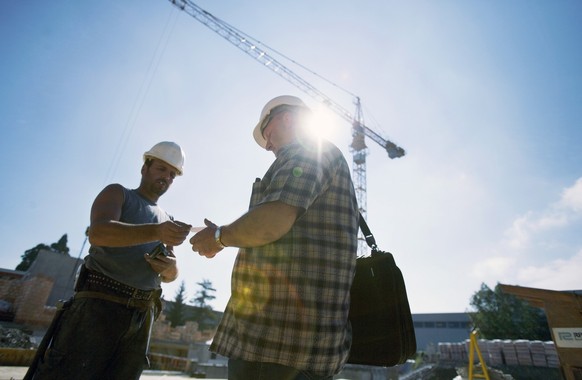Ein Kontrolleur prueft am 17. August 2005 auf einer Baustelle in Bern die Arbeitsbewilligung eines Arbeiters auf einer Baustelle. Damit soll die Garantie des Arbeitsnehmers auf Renten- und Versicherun ...