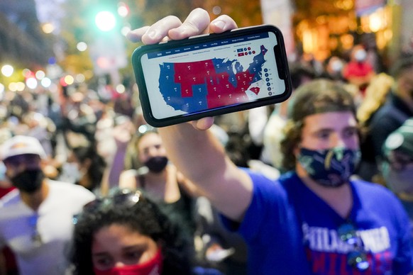 A supporter of President-elect Joe Biden holds up his mobile phone to display the electoral college map outside the Philadelphia Convention Center after the 2020 Presidential Election is called, Satur ...