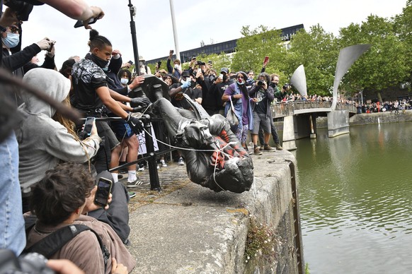 Protesters throw a statue of slave trader Edward Colston into Bristol harbour, during a Black Lives Matter protest rally, in Bristol, England, Sunday June 7, 2020, in response to the recent killing of ...