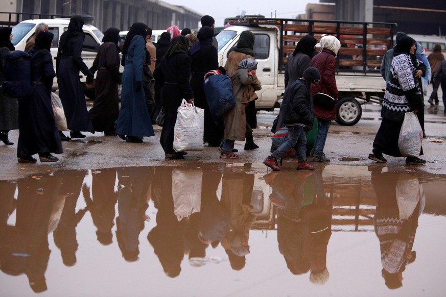 Syrians evacuated from eastern Aleppo walk with their belongings near a puddle of water in government controlled Jibreen area in Aleppo, Syria November 30, 2016. REUTERS/Omar Sanadiki