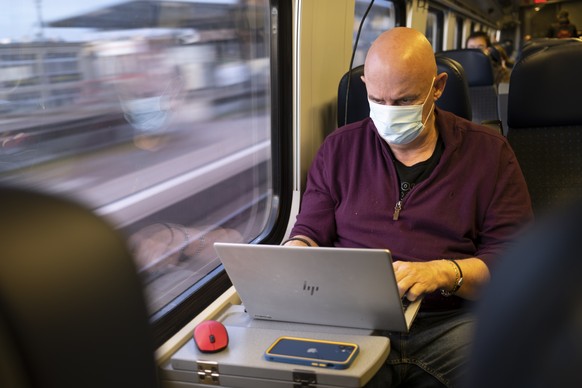Passenger wearing protective mask works on a laptop as he rides a SBB CFF FFS train during the coronavirus disease (COVID-19) outbreak, in Neuchatel, Switzerland, Tuesday, March 23, 2021. Switzerland  ...
