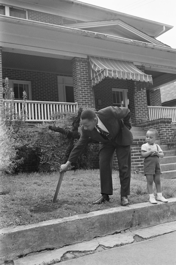 Using one hand, integration leader Reverend Martin Luther King Jr. pulls up the four foot cross that was burned on the front lawn of his home on April 26th. With King is his son Martin Luther III, 2.  ...