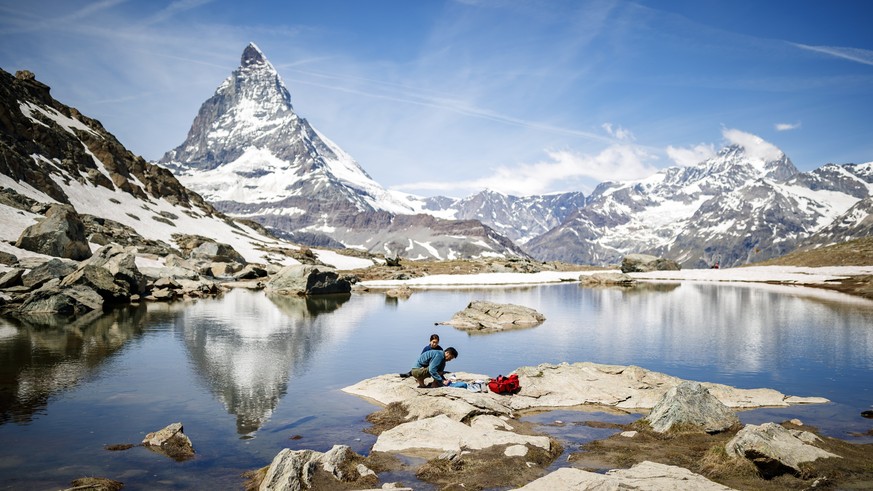 epa06830580 Tourists rest by a pond in front of the the iconic Matterhorn mountain, peaking at 4478m, as they hike in the Riffelberg area above the alpine village of Zermatt, Switzerland, 22 June 2018 ...