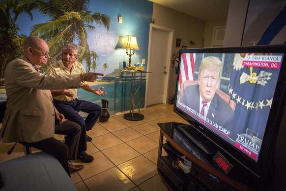 epa07270458 Miguel Saavedra (R) and his friend Oswaldo Hernandez (L) watch US President Donald J. Trump on TV, from their home in Miami, Florida, USA, 08 January 2019. President Trump deliverd an addr ...