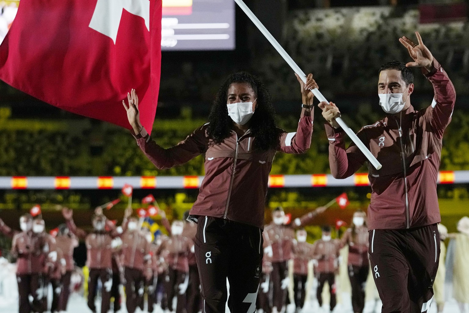 Mujinga Kambundji and Max Heinzer, of Switzerland, carry their country&#039;s flag during the opening ceremony in the Olympic Stadium at the 2020 Summer Olympics, Friday, July 23, 2021, in Tokyo, Japa ...